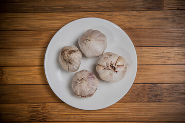 garlic on white plate, wood background, ingredient seasoning herb vegetable