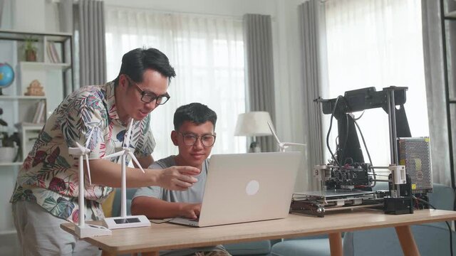 Cheerful Father And His Son Using Laptop Computer Programming Electric Wind Turbine Model And 3D Printer At Home
