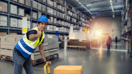 Warehouse  worker pulling a pallet truck and taking or upload package box to shelf in large warehouse. Active caucasian man showing thump up and looking at camera with smiling.