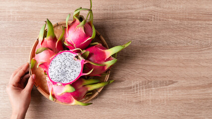Dragon fruit or pitaya in a basket holding by woman hand on woden background, Tropical fruit, Table top view