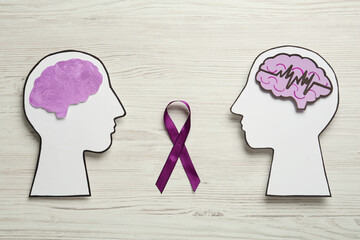 Human head cutouts with different brains and purple ribbon on white wooden background, flat lay....