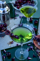 Green Apple vodka cocktail with lemon lime juice in stemware drinking glasses and garnished with raw ripe cherry halves on bamboo skewer 