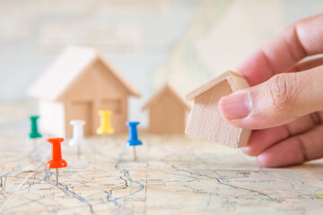 Selective focus of red pin and hand holding house model on map background  for real estate concept