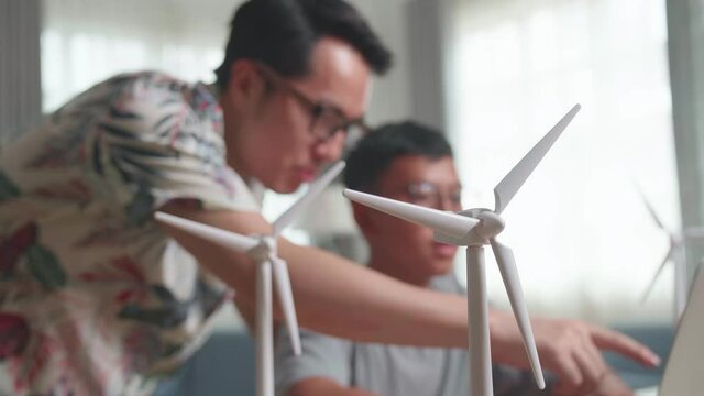 Wind Turbine Model And Blur Teacher Teaching Boy Use Laptop Computer 
