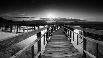 Obraz premium perspective of wood bridge in deep sea crossing water stream and glowing light at the end of wooden ways