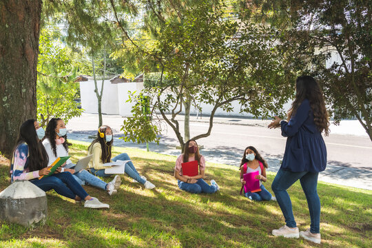 Teacher teaching outdoor classes to a group of Latina teenage students wearing a mask and social distancing due to the coronavirus pandemic