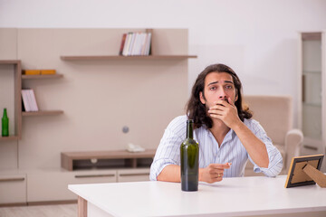 Young man drinking alcohol at home in unhappy love concept