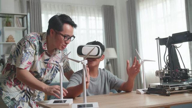 Asian Father Teach His Son While Wearing Vr Glasses With Electric Wind Turbine Model And 3D Printer At Home
