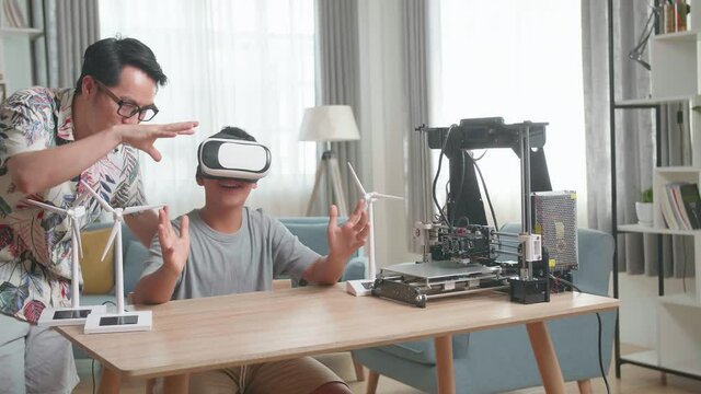 Asian Father Teach His Son While Wearing Vr Glasses With Electric Wind Turbine Model And 3D Printer At Home
