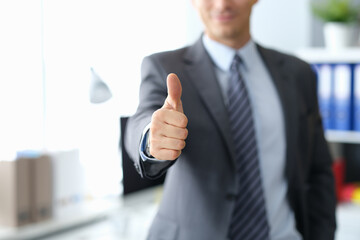 Businessman showing thumbs up gesture while standing in office