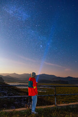 Fototapeta na wymiar noise in the universe with grain Long exposure photography night light, Man wearing winter cloth standing next to the pointing the milky way with a flashlight