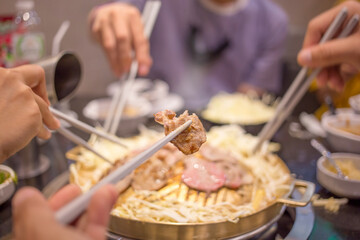 In hand with the Grill pork on wooden chopsticks, Thai bbq Barbecue on a hot pan, grilled pork on a hot stove  holiday  family eating at a restaurant