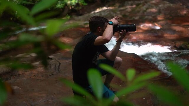 Adventure photographer getting the perfect angle and composition to take a picture of a waterfall - slow motion