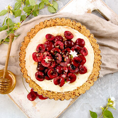 Cherry vanila tart topped with berries on light gray background.