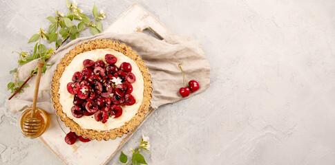 Cherry vanila tart topped with berries on light gray background.