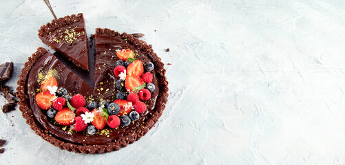 Young woman holding homemade chocolate tart on light gray background.