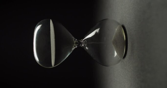 A sand clock slowly rotating on black background. Abstract running time concept.