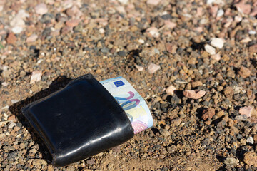 Black wallet on dirt ground with twenty euros note bill. Lost money, luck concepts