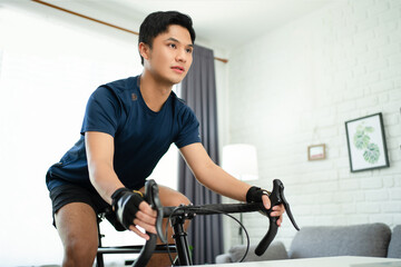 Naklejka na ściany i meble Asian man cycling a bicycle on a trainer at house in the morning. Health and lifestyle concepts.