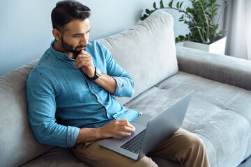 Portrait of thoughtful indian businessman touching chin looking at laptop screen