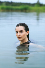Fototapeta premium A dark-haired girl swims in the lake and takes a photo session