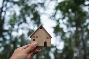 Closeup image of a hand holding and showing wooden house model with nature background