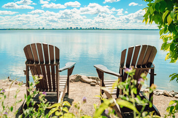 Two Muskoka chairs by the water on home terrace with calm view of lake in Canada. Summer cottage...