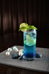 iced blue island cooler soda mocktail with lime and mint leaf kombucha in glass on bar counter dark...