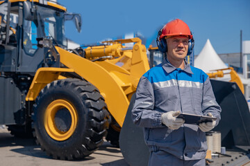 Smart construction site, foreman in helmet controls equipment using computer tablet and Internet