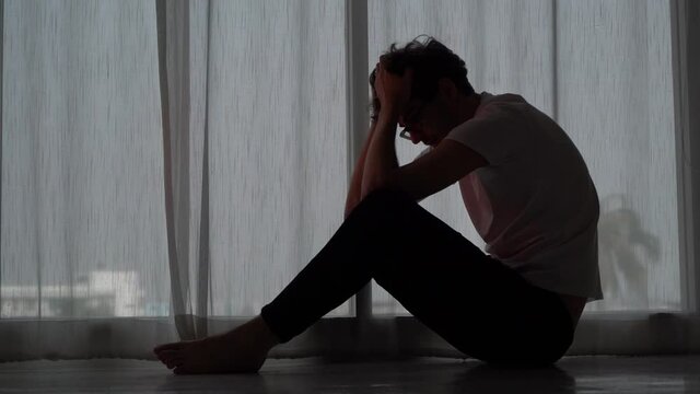Desperate man sitting with hands on his head on the floor beside windows for stress and depression concept.