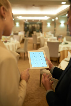 Banquet Manager Discussing Seating Plan On Tablet Computer With Restaurant Head Waiter