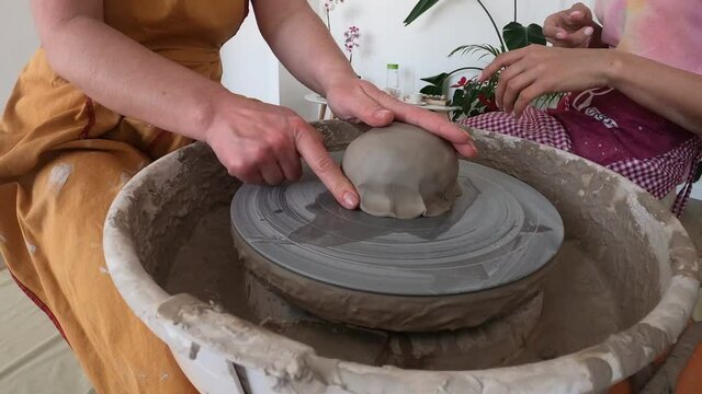 Women working on the potter's wheel. Hands of teacher show to student how to hold and push clay. Girl sculpt cup from white clay pot. Workshop on modeling do plate. Concept: handmade, workshop, artist