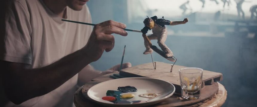 Artist paintbrush paints skateboarder art sculpture in atelier studio
