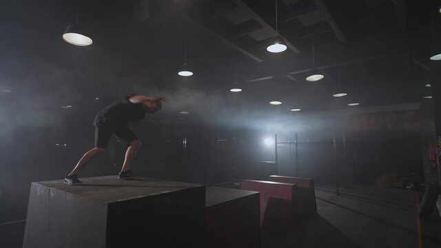 Free running, young man doing a series of somersaults on the training ground for parkour and workout, guy perform flips and gymnastic tricks in a dark space, 4k slow motion.
