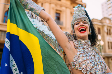 Beautiful Brazilian woman wearing colorful Carnival costume and Brazil flag during Carnaval street...