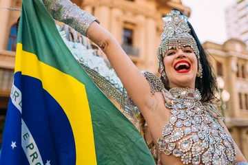 Poster Beautiful Brazilian woman wearing colorful Carnival costume and Brazil flag during Carnaval street parade in city. © Brastock Images