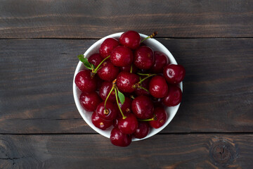 Ripe fresh cherry berries in a plate, dark rustic wooden background. Copy space.