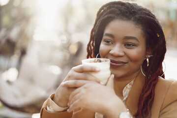 Beautiful young african american woman sitting in outdoor cafe and drinking coffee