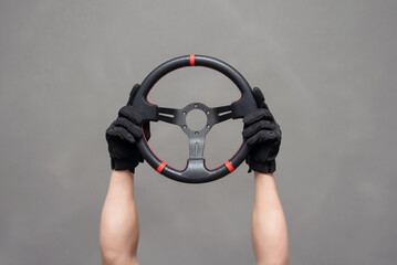 A sport car steering wheel in a driver hands raised up on the gray background.