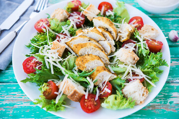 Caesar salad with chicken breast on a rustic background, tomatoes, parmesan, green salad and croutons, selective focus - obrazy, fototapety, plakaty