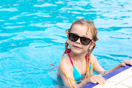 caucasian child girl in sunglasses in an outdoor swimming pool on a summer day