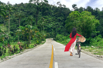 Beautiful young woman in traditional Vietnamese dress Ao Dai walking by the road at jungle forest