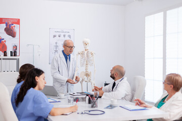 Therapist senior man discussing bone structure analyzing anatomy body skeleton presenting medical expertise. Hospital team working at diagnosis examination in conference meeting room