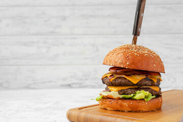 Double cheeseburger served on wooden board against white blurred background - obrazy, fototapety, plakaty