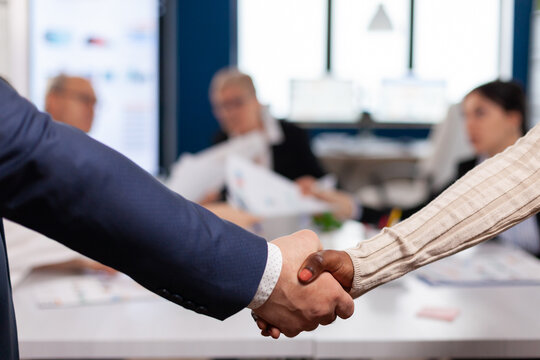 Close up of multiracial business partners standing in front of conference desk shaking hands after signing partnership contract. Diverse team being happy for successful negotiations in startup company