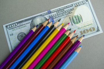multicolored pencils on souvenir dollar bills. items lie on a gray background