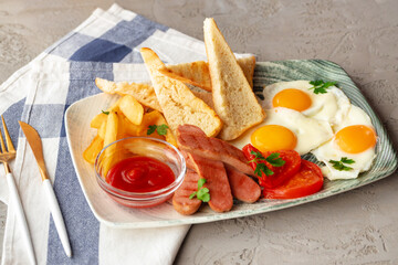 English breakfast with eggs, sausages, french toasts and potato wedges on gray table