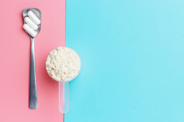 Protein scoop and capsules on pink and blue background close-up.