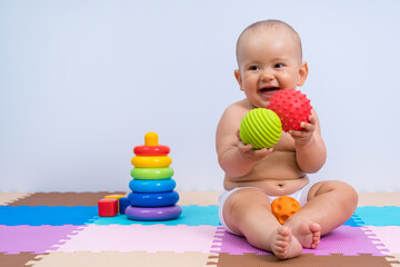 Happy newborn baby playing with rubber balls in playroom