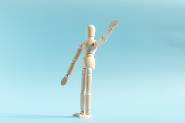 The figure of a wooden man with his hand raised up . The figure of a wooden man on a colored background of kopi space